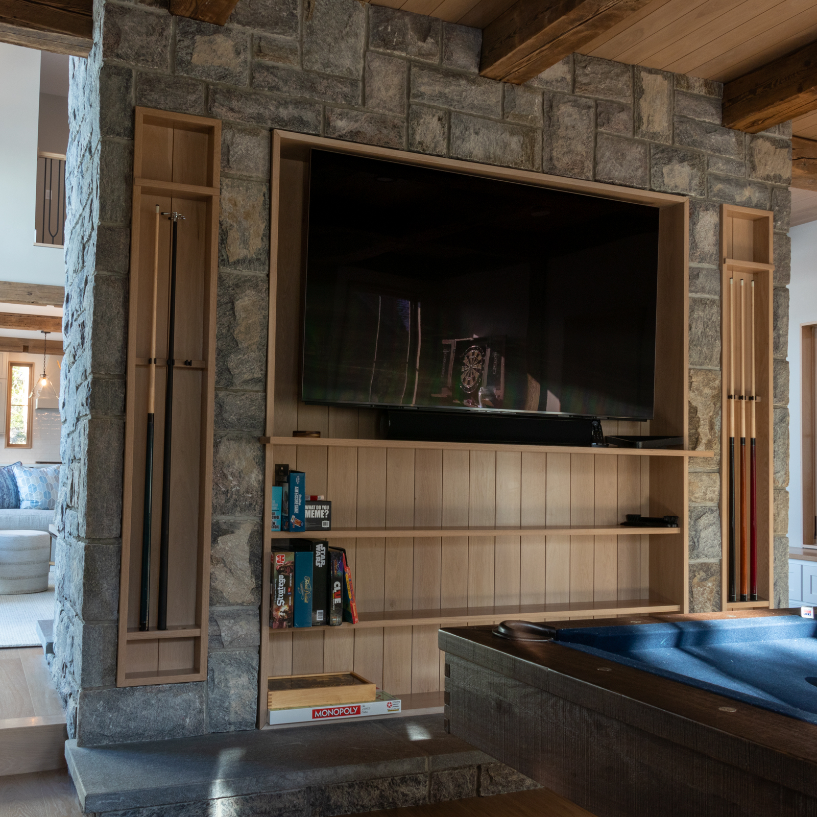 This space features a pool table, dart area, and custom game storage on the back side of the fireplace. The storage area was custom built out of white oak to hold pool cues, books & board games, pool accessories, and a large tv for watching the game while you play a round with some friends.